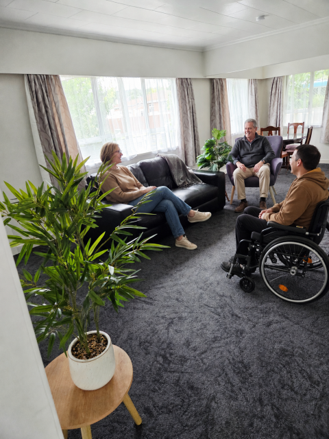 Three guests relaxing together in the lounge, including a wheelchair user.